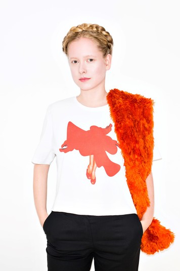 Анна Октябрь в футболке Николая Карабиновича. Принт Николая Карабиновича демонстрирует красоту как она есть: красивые женские ноги, туфли на каблуках, разлетающаяся алая юбка. Яркий красный цвет тут является одновременно как символом красоты, так и символом нависшей опасности – скоротечности той самой красоты.