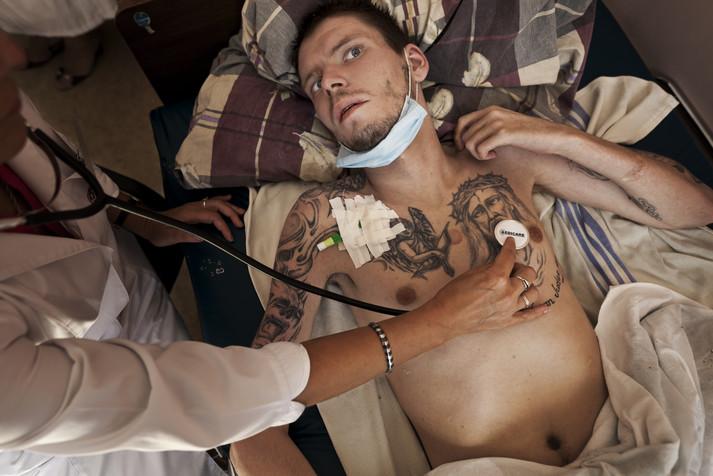 Киевский городской ценр СПИДа.
Киев, август 2011.
Денис, 26 лет. ВИЧ-позитивный, болен туберкулезом. Раньше он был социальным работником. Трижды попадал в СИЗО, в последний раз за кражу и разбой. Был переведен из СИЗО в СПИД-центр из-за сильного ухудшения состояния здоровья. Потерял речь и не может двигаться. Несмотря на тяжелое состояние и то, что он фактически умирает, Денис прикован наручниками к кровати и находится под конвоем милиции. Эта клиника – одна из лучших в Украине и работает со многими наркозависимыми и другими сложными ВИЧ-инфицированными пациентами, поэтому в клинике существуют жесткие правила и условия, которые необходимы для безопасности самих пациентов и медицинского персонала.